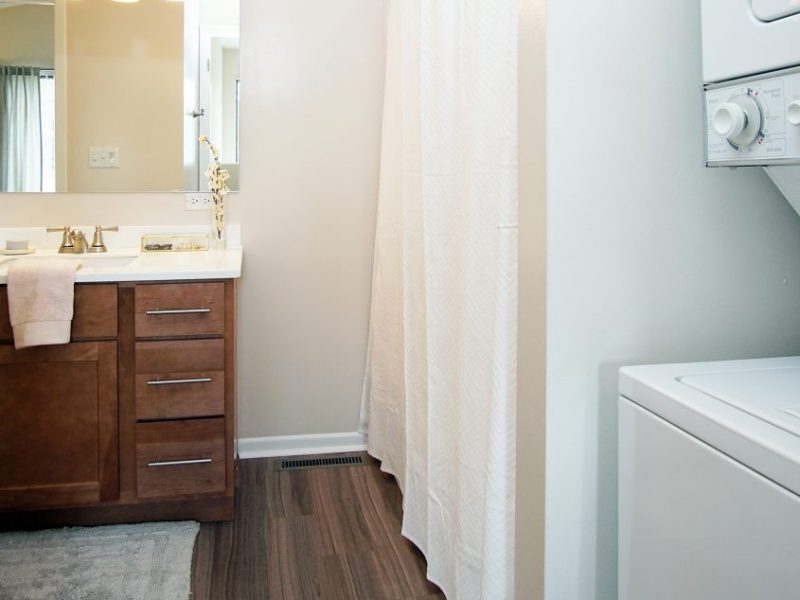 This image exhibits the bathroom area showcasing the wood shaker style cabinets and trendy laminate plank flooring for an ideal amenity.