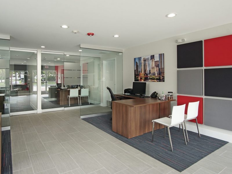 This image shows a spacious inside view of the leasing center featuring a wooden table, chair, and computer.